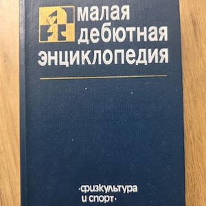 May include: A navy blue book with the title "малая дебютная энциклопедия" in white lettering. The book has a gold and black logo in the upper left corner and the text "физкультура и спорт" at the bottom.