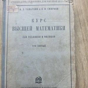Puede incluir: Un libro antiguo con una cubierta gris descolorida. El título "KURS VYSHEI MATEMATIKI" se muestra de forma destacada, junto con los nombres de los autores y la editorial. El libro se titula "TOM PERVYI" y fue publicado en 1927.
