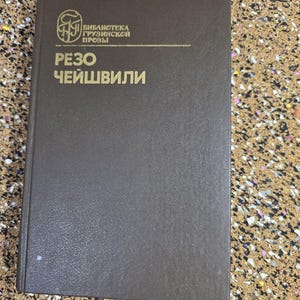 May include: A brown book with gold lettering and text in a foreign language. The book's cover features a logo and the title "РЕЗО ЧЕЙШВИЛИ". The book is closed and appears to be in good condition.