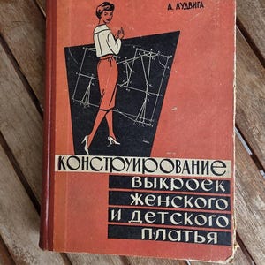 May include: A vintage hardcover book with a red cover featuring a black geometric pattern and an illustration of a person in a white top and red skirt. The text reads A. ЛУДВИГА, КОНСТРУИРОВАНИЕ ВЫКРОЕК ЖЕНСКОГО И ДЕТСКОГО ПЛАТЬЯ in black and white lettering.