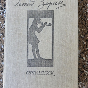 May include: A vintage book with a light beige cover. The title and author's name are in cursive script at the top. A black silhouette of a person playing a wind instrument is in the center, with the title "СТРАННИК" below.