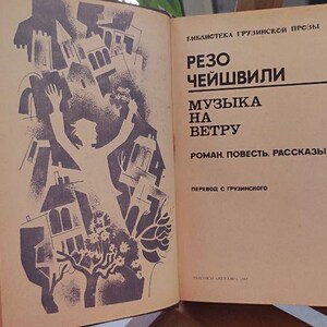 May include: An open book with a vintage cover featuring a purple and white illustration of a figure surrounded by buildings. The right page has text in Russian. The book is on a wooden surface near a potted plant.