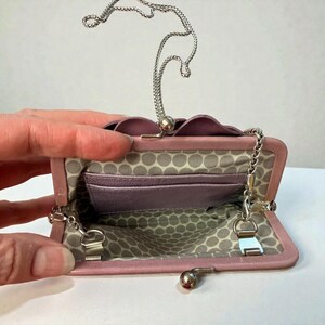 Puede incluir: Un peque&ntilde;o bolso abierto de color lavanda con una correa de cadena plateada. El interior presenta un forro estampado y varios compartimentos. El bolso tiene un cierre de broche y un borde festoneado decorativo.
