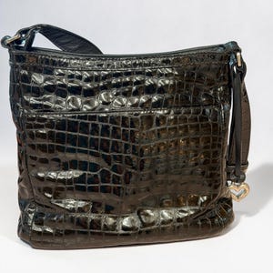 May include: A black shoulder bag with a glossy, embossed crocodile skin texture. The bag features a rectangular silhouette, a top zipper closure, and a silver-toned metal heart-shaped charm attached to the side strap hardware.