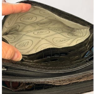 May include: A black handbag with a glossy, textured crocodile-embossed exterior. The interior is lined with a light-colored fabric featuring a repeating pattern of the letter B inside an oval shape, separated by thin, dashed horizontal lines.