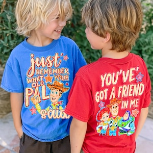 Peut inclure: Un t-shirt bleu avec le texte "just remember what your old pal said" et une illustration de Woody, et un t-shirt rouge avec le texte "YOU'VE GOT A FRIEND IN ME" montrant des illustrations de Jessie, Woody et Buzz l'Éclair.