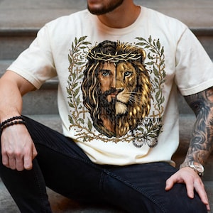 May include: Cream-colored t-shirt featuring a split graphic of Jesus and a lion. The design includes a crown of thorns, a butterfly, and the text "SIMPLY SMOOTH DESIGNS". The artwork is framed by a leafy border.