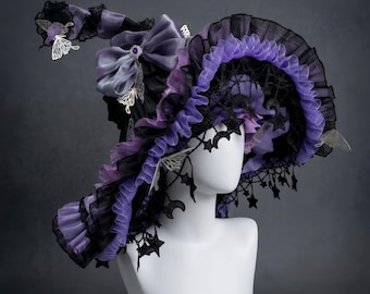 Puede incluir: Un sombrero de bruja caprichoso en negro y morado, adornado con volantes, lazos y detalles de mariposas. El sombrero presenta un ala ancha con detalles de encaje y estrellas, presentado sobre una cabeza de maniquí blanca. Diseño elegante y caprichoso.