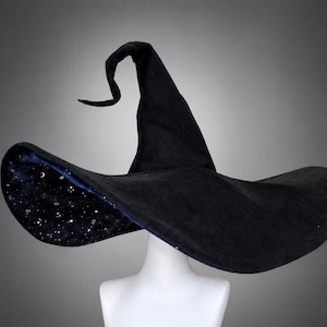 May include: A black pointed hat with a wide brim and a curved top. The underside of the brim features a dark blue fabric printed with a pattern of white stars and crescent moons, contrasting with the solid black exterior of the hat.
