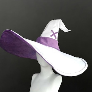 May include: A white pointed hat with a wide brim, featuring a purple band around the base and a purple cross symbol on the front of the cone. The underside of the wide brim is a solid purple color, contrasting with the white exterior of the hat.