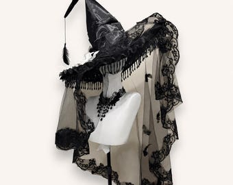 May include: A black pointed hat with a wide brim, featuring intricate lace trim, hanging fringe, and a long sheer veil with floral lace edges. A matching black lace choker with dangling teardrop accents is displayed on a white mannequin neck.