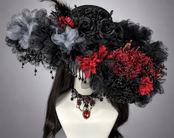 May include: A wide-brimmed black hat adorned with black and grey fabric flowers, red floral accents, black lace, feathers, and hanging black beads. A matching black lace choker necklace with red teardrop-shaped crystals is displayed below.