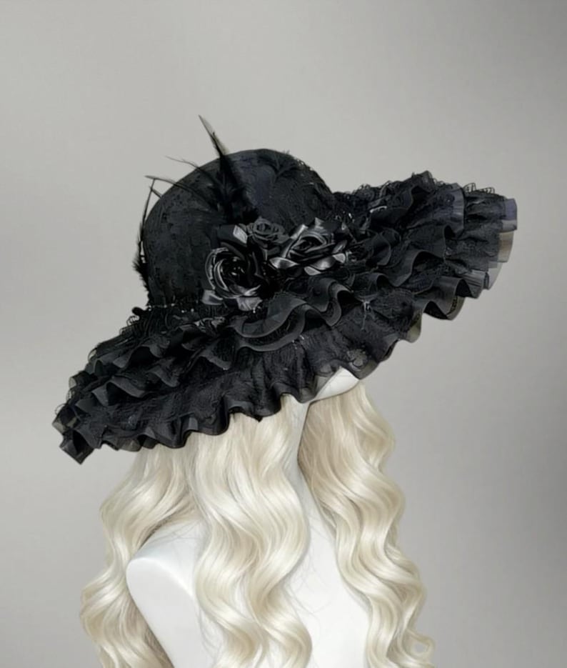 May include: A black, wide-brimmed hat with a ruffled lace brim and decorative black roses. The hat features a high crown and is adorned with feathers. The hat is displayed on a mannequin head with long, wavy, blonde hair.