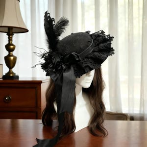 May include: A black hat with a decorative design, featuring lace trim, feathers, and a large bow. The hat is displayed on a mannequin head, showcasing its intricate details and elegant style. The hat is a vintage style accessory.