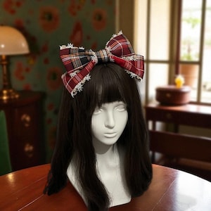 Może przedstawiać: Czerwono-czarna i biała kraciasta opaska do włosów z białą koronkową lamówką. Duża kokarda znajduje się na głowie manekina z długimi, ciemnymi włosami. Modny dodatek do włosów.