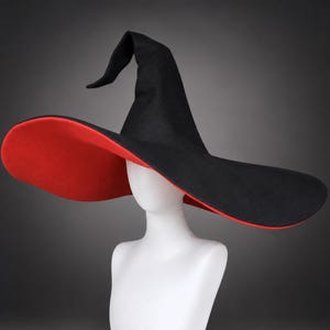 Könnte beinhalten: Ein hoher, spitzer Hexenhut mit schwarzer Außenseite und leuchtend roter Unterseite. Der Hut hat eine breite, flexible Krempe, die sich an der Spitze leicht biegt, und besteht aus einem filzartigen Material mit einer glatten, matten Oberfläche.