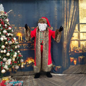 Puede incluir: Una persona con un disfraz de Papá Noel, con un abrigo rojo con ribete de piel sintética, un gorro a juego y guantes negros. El disfraz incluye una barba blanca y una camisa a cuadros. Un árbol de Navidad decorado está a la izquierda.