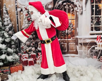 Könnte beinhalten: Weihnachtsmann in einem roten Anzug mit weißer Verzierung, einem schwarzen Gürtel mit goldener Schnalle und einer roten Mütze. Er trägt einen großen roten Sack über der Schulter. Der Hintergrund zeigt eine verschneite Szene.