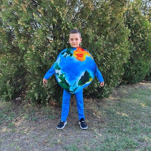 Può includere: Un bambino indossa un costume blu della Terra, composto da una maglia blu a maniche lunghe e pantaloni. Il costume della Terra presenta oceani blu e continenti in verde, giallo e arancione. Il bambino indossa scarpe da ginnastica nere.