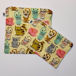 May include: Two yellow fabric zippered pouches with a cat theme. The pouches are decorated with colorful cats and the words "bengal", "siamese", "persian", "maine coon", "tabby", and "blue".