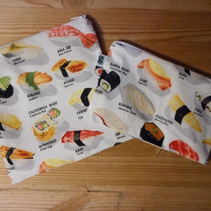 May include: Two white zippered pouches with colorful illustrations of different types of sushi. The pouches are labeled with the names of the sushi, such as "Saba", "Ama Ebi", "Kappa Maki", "Sake", "Kani", "Ebi", "Tako", and "Kazunoko".
