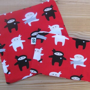 May include: Two red fabric pouches with a white and black ninja pattern. The pouches are lined with a green fabric and have a white tag with the word "SO" on it.