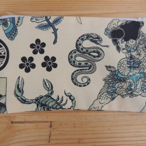 May include: A beige zippered pouch with a Japanese-inspired design. The pouch features a variety of traditional Japanese tattoo motifs, including a snake, a scorpion, a flower, and a wave. The pouch is perfect for storing small items like makeup, jewelry, or coins.