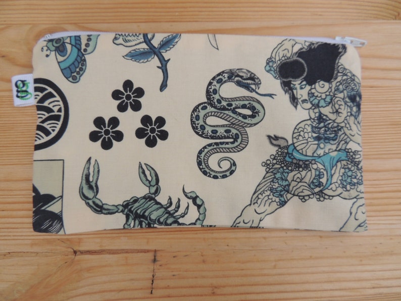 May include: A beige zippered pouch with a Japanese-inspired design. The pouch features a variety of traditional Japanese tattoo motifs, including a snake, a scorpion, a flower, and a wave. The pouch is perfect for storing small items like makeup, jewelry, or coins.