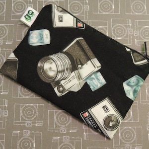 May include: Black zippered pouch with a repeating pattern of vintage cameras and ice cubes. The pouch is made of fabric and has a zipper closure.