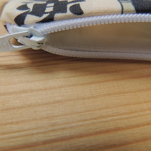 May include: A white zipper with a white zipper pull on a beige fabric pouch with black and white patterns.
