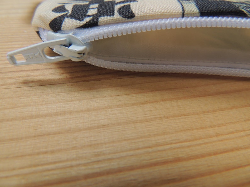 May include: A white zipper with a white zipper pull on a beige fabric pouch with black and white patterns.