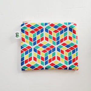 May include: A white zippered pouch with a geometric pattern of red, blue, yellow, and green cubes. The pouch has a white zipper and a green label with the text "GO!" on it.