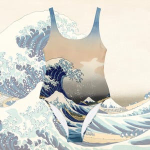 以下が含まれることがあります： 葛飾北斎の「神奈川沖浪裏」のプリントが施されたワンピース水着。水着は丸いネックラインとハイカットの脚を備えています。デザインは青、白、ベージュの色合いで、背景に山があります。