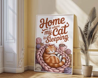 May include: A rectangular wall art print featuring a sleeping orange tabby cat curled inside a large pink chunky knit basket. The text reads Home is where my Cat is Sleeping. Several balls of yarn and a steaming mug of cocoa are also illustrated.