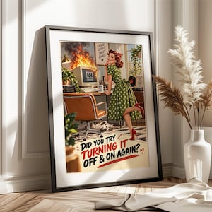 Op de afbeelding: Een ingelijste kunstdruk met een retro-illustratie van een persoon in een groene jurk met stippen naast een brandende computermonitor. De tekst luidt: "DID YOU TRY TURNING IT OFF & ON AGAIN?" met een klein rood hartje.