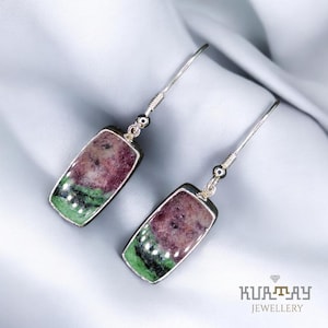 Könnte beinhalten: Ein Paar rechteckige Ohrhänger. Jeder Ohrring hat einen silbernen Rahmen, der einen Stein mit tiefroten, grünen und schwarzen Farbtönen umgibt. Die Ohrringe haben ein schlichtes, elegantes Design, das sich für den täglichen Gebrauch eignet.