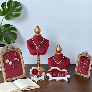Puede incluir: Juego de exhibición de joyas con un busto de terciopelo burdeos, una exhibición con marco dorado y sofás blancos en miniatura. El busto muestra un collar de perlas. El conjunto incluye aretes, anillos y collares.