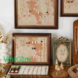May include: A display of various jewelry pieces, including necklaces, earrings, and bracelets. The jewelry is presented in framed displays and a wooden jewelry box. The pieces are gold-toned and feature gemstones and decorative elements. The image includes the text "VintGlim".