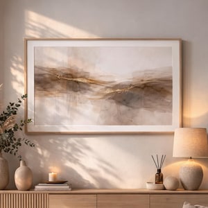 Könnte beinhalten: Ein gerahmtes abstraktes Aquarellgemälde in neutralen Tönen von Beige, Braun und Gold. Das Kunstwerk zeigt ein landschaftsähnliches Design mit weichen, gemischten Farben und goldenen Akzenten. Der Rahmen hat eine helle Holzfarbe.