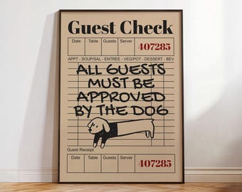 May include: A framed print featuring a tan background with black text that reads "Guest Check." The text "ALL GUESTS MUST BE APPROVED BY THE DOG" is written in a handwritten style. A cartoon dog illustration is at the bottom.