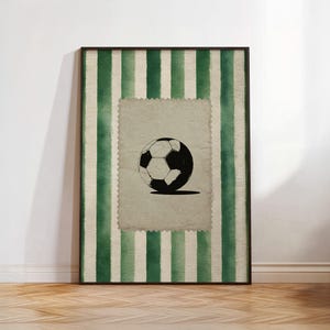 Könnte beinhalten: Gerahmter Kunstdruck mit einer schwarz-weißen Fußballillustration auf einem Hintergrund im Vintage-Stil. Der Fußball befindet sich auf einem strukturierten, cremefarbenen Rechteck, das von grünen und weißen vertikalen Streifen umrahmt und in einem schwarzen Rahmen eingefasst ist.
