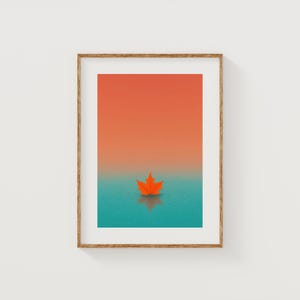 May include: Framed art print featuring an orange maple leaf floating on teal water. The background transitions from orange to teal, creating a serene and minimalist landscape. The artwork is encased in a wooden frame.