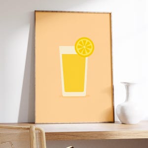 Puede incluir: Un cuadro enmarcado con una bebida amarilla en un vaso alto con una rodaja de limón. La obra de arte tiene un estilo minimalista con un fondo naranja claro. Un jarrón blanco está sobre una superficie de madera.