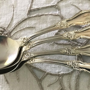 May include: Four silver spoons with ornate floral designs on the handles. The spoons are stacked on top of each other, with the bowls facing up.