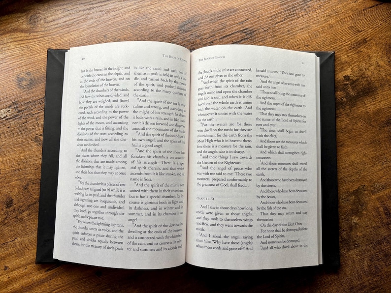 Puede incluir: Un libro de tapa dura abierto con p&aacute;ginas blancas y texto impreso en negro. La p&aacute;gina izquierda se titula The Book of Enoch y contiene varios p&aacute;rrafos de texto. La p&aacute;gina derecha contin&uacute;a el texto e incluye el encabezado Chapter 61.