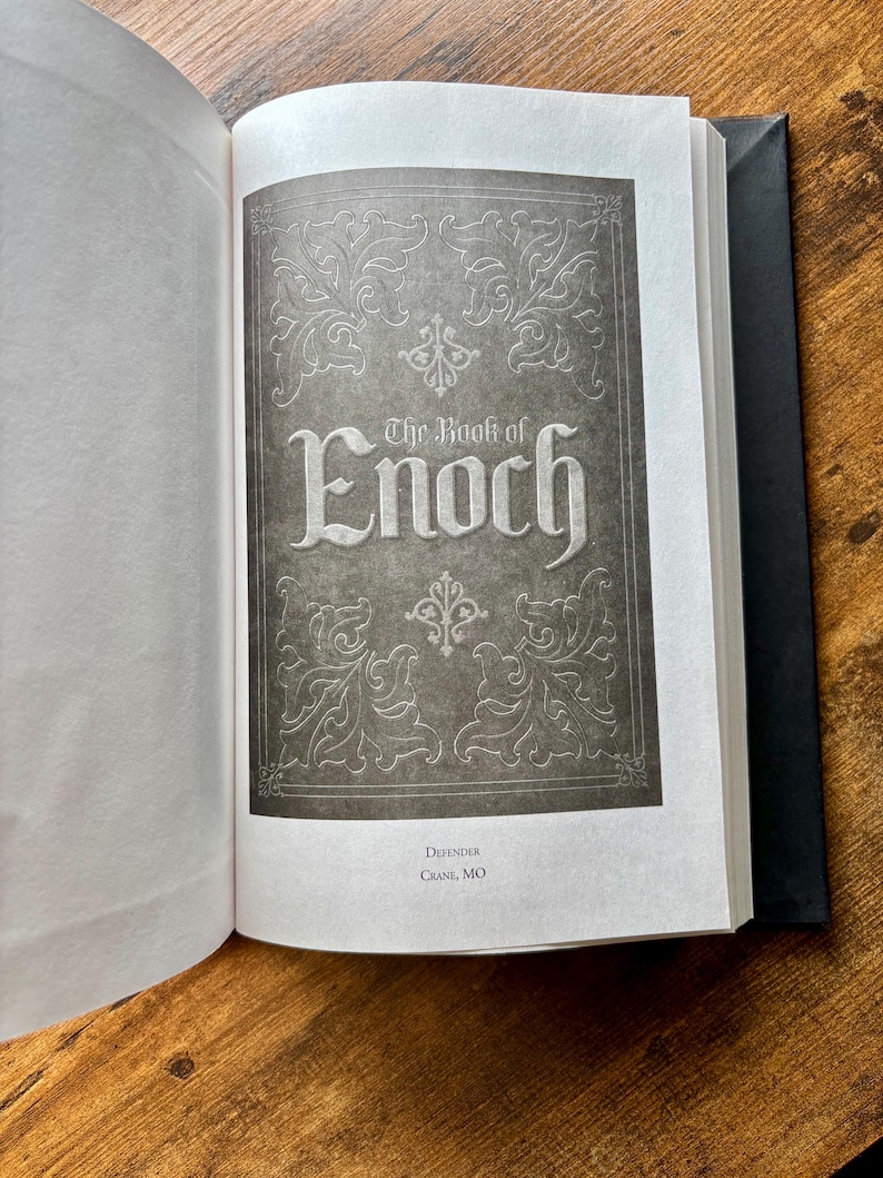 Puede incluir: Un libro de tapa dura abierto que muestra una p&aacute;gina de t&iacute;tulo con el texto The Book of Enoch en una fuente estilizada. La p&aacute;gina presenta un fondo gris oscuro con bordes florales decorativos blancos y el texto Defender Crane, MO abajo.