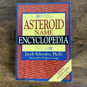 May include: A hardcover book titled "Asteroid Name Encyclopedia" by Jacob Schwartz, Ph.D. The cover is blue with yellow and white text, and a star graphic. Includes a "Personal Asteroid Chart!" insert.
