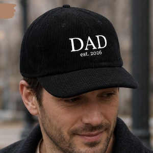 Puede incluir: Una gorra de béisbol de pana negra con el texto bordado en blanco DAD y est. 2026 centrado en el panel frontal. La gorra presenta una corona estructurada, una visera curva y un acabado de tela texturizada de diseño clásico.