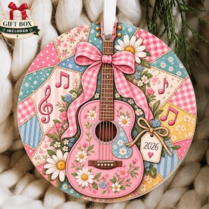 May include: A round ceramic ornament featuring a pink acoustic guitar decorated with white daisies and green leaves. The background is a patchwork of pink, blue, and yellow floral and gingham patterns with musical notes and a tag labeled 2026.