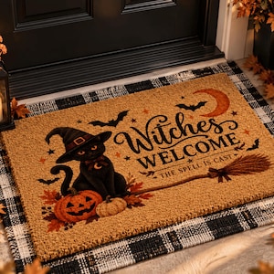 May include: A rectangular tan coir doormat featuring a black cat wearing a witch hat, a jack-o'-lantern, a broomstick, bats, and a crescent moon. The text reads Witches WELCOME THE SPELL IS CAST, surrounded by small stars and autumn leaves.
